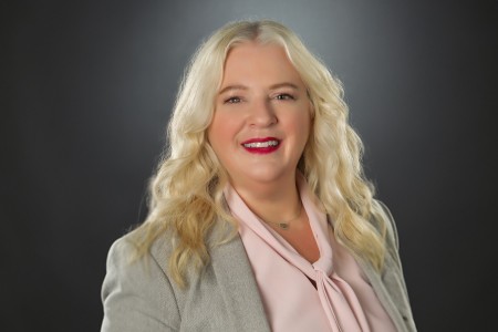 Dorothy Lockhart, a caucasian blonde woman, wearing light pink top with grey blazer, red lipsticks and smile