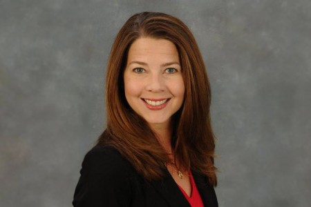 Emily Cox, a woman wearing red top with black blazer, grey eyes, brown hair, brown lipstick with big smile